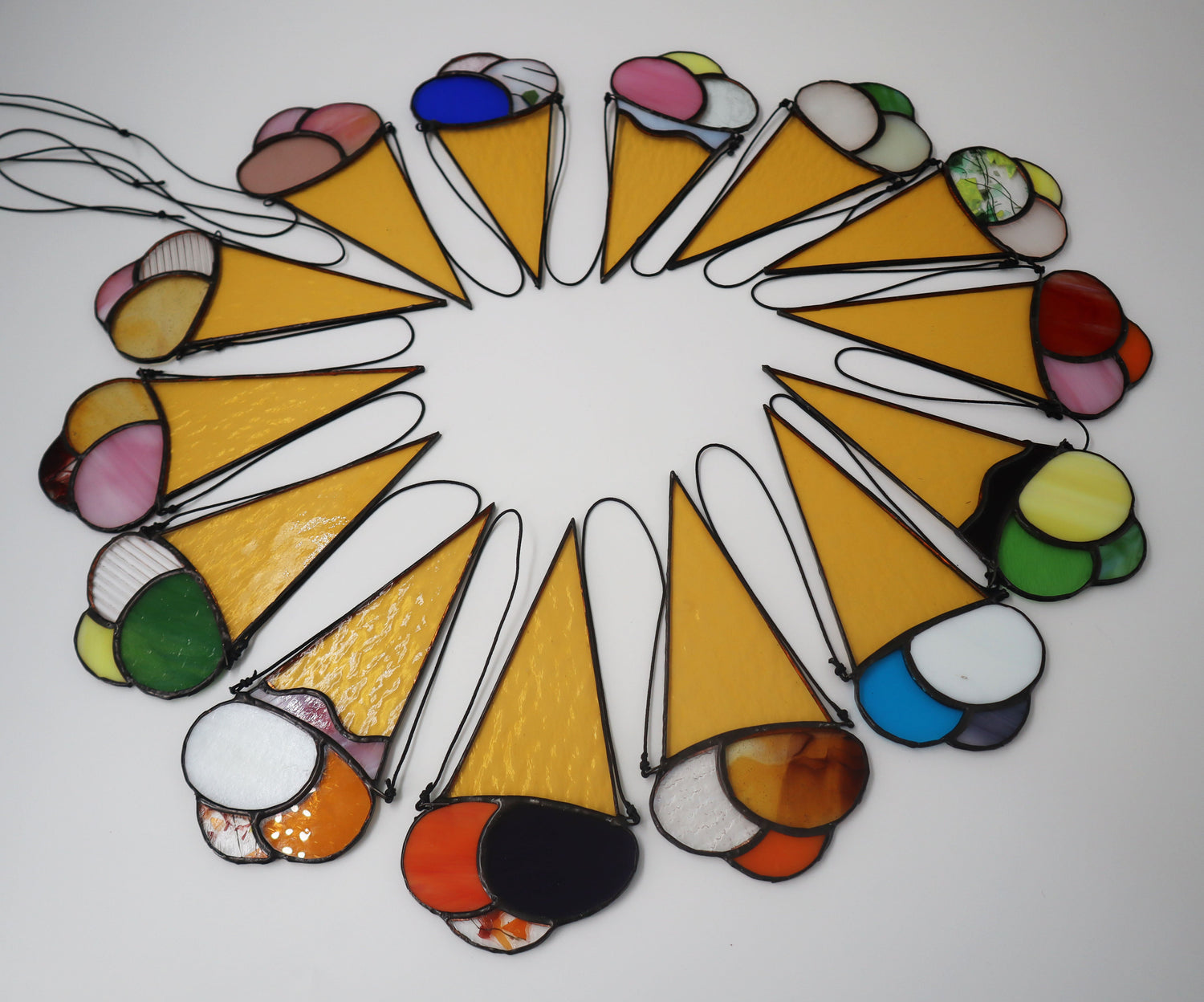 Stained glass art pieces shaped like ice cream cones, arranged in a circle. The cones are yellow with various colored scoops, including pink, blue, red, and green.