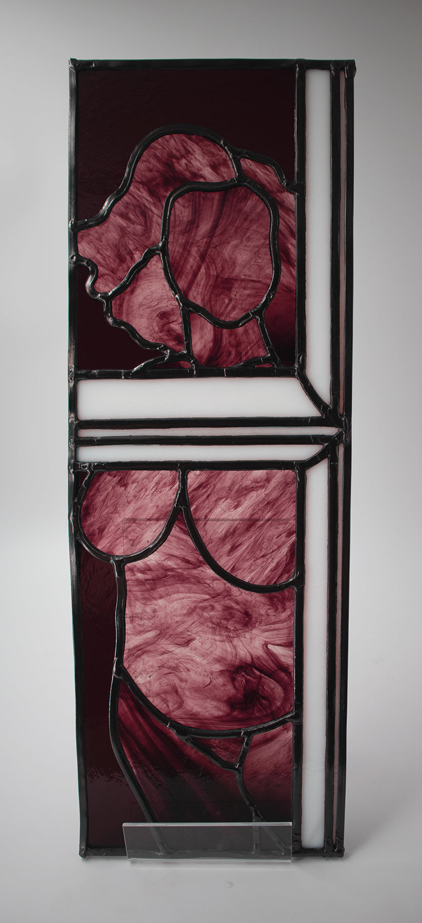 Alfreda, another example of LF Kaleidoscope’s Stained Glass Portraits. This stunning artwork captures the life model reflected in a bedroom window. Alfreda’s portrait showcases her flowing hair, and beautiful torso shapes rendered in deep red, luxuriant purples with the black lead lines creating structure and definition against the white glass window frame. Alfreda is staring through the window at you, and would look excellent in any house or gallery.