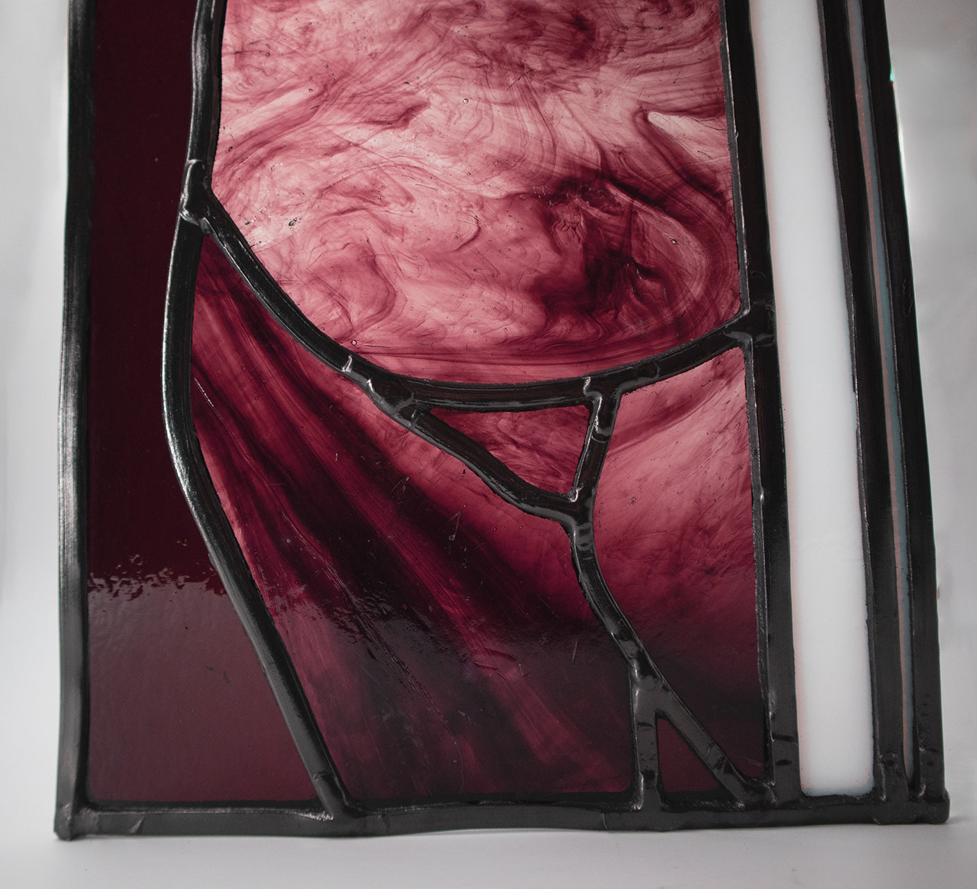 Alfreda, another example of LF Kaleidoscope’s Stained Glass Portraits. This stunning artwork captures the life model reflected in a bedroom window. Alfreda’s portrait showcases her flowing hair, and beautiful torso shapes rendered in deep red, luxuriant purples with the black lead lines creating structure and definition against the white glass window frame. Alfreda is staring through the window at you, and would look excellent in any house or gallery.