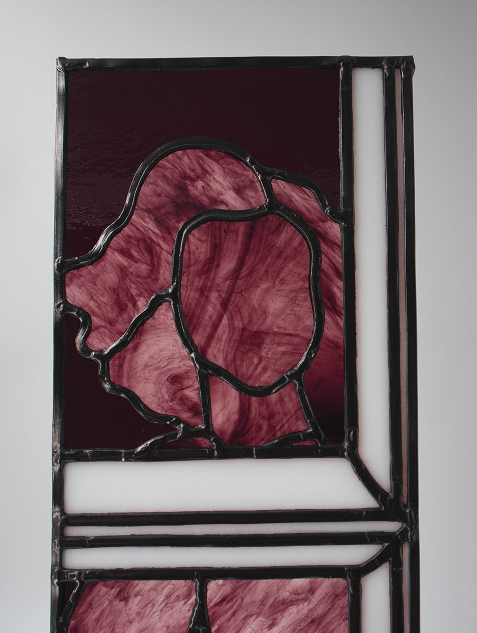 Alfreda, another example of LF Kaleidoscope’s Stained Glass Portraits. This stunning artwork captures the life model reflected in a bedroom window. Alfreda’s portrait showcases her flowing hair, and beautiful torso shapes rendered in deep red, luxuriant purples with the black lead lines creating structure and definition against the white glass window frame. Alfreda is staring through the window at you, and would look excellent in any house or gallery.