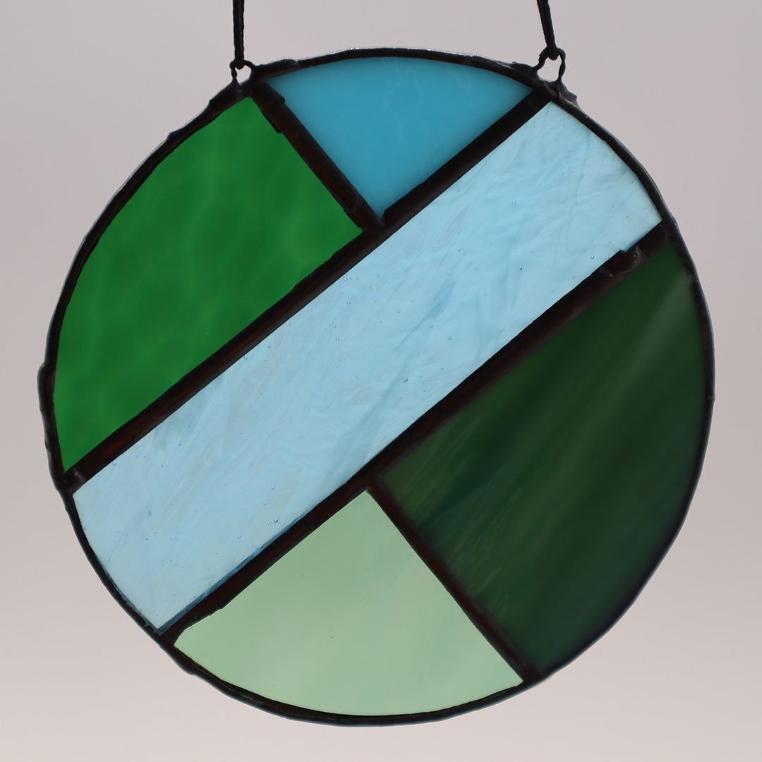 Four distinct pieces from the "Circles, Green" collection by LF Kaleidoscope are showcased against a white backdrop. Each suspended circle displays geometric patterns in hues of green and blue, with diverse textures. They are affixed to black strings for hanging.