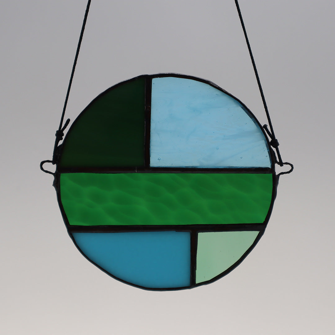 Four distinct pieces from the "Circles, Green" collection by LF Kaleidoscope are showcased against a white backdrop. Each suspended circle displays geometric patterns in hues of green and blue, with diverse textures. They are affixed to black strings for hanging.