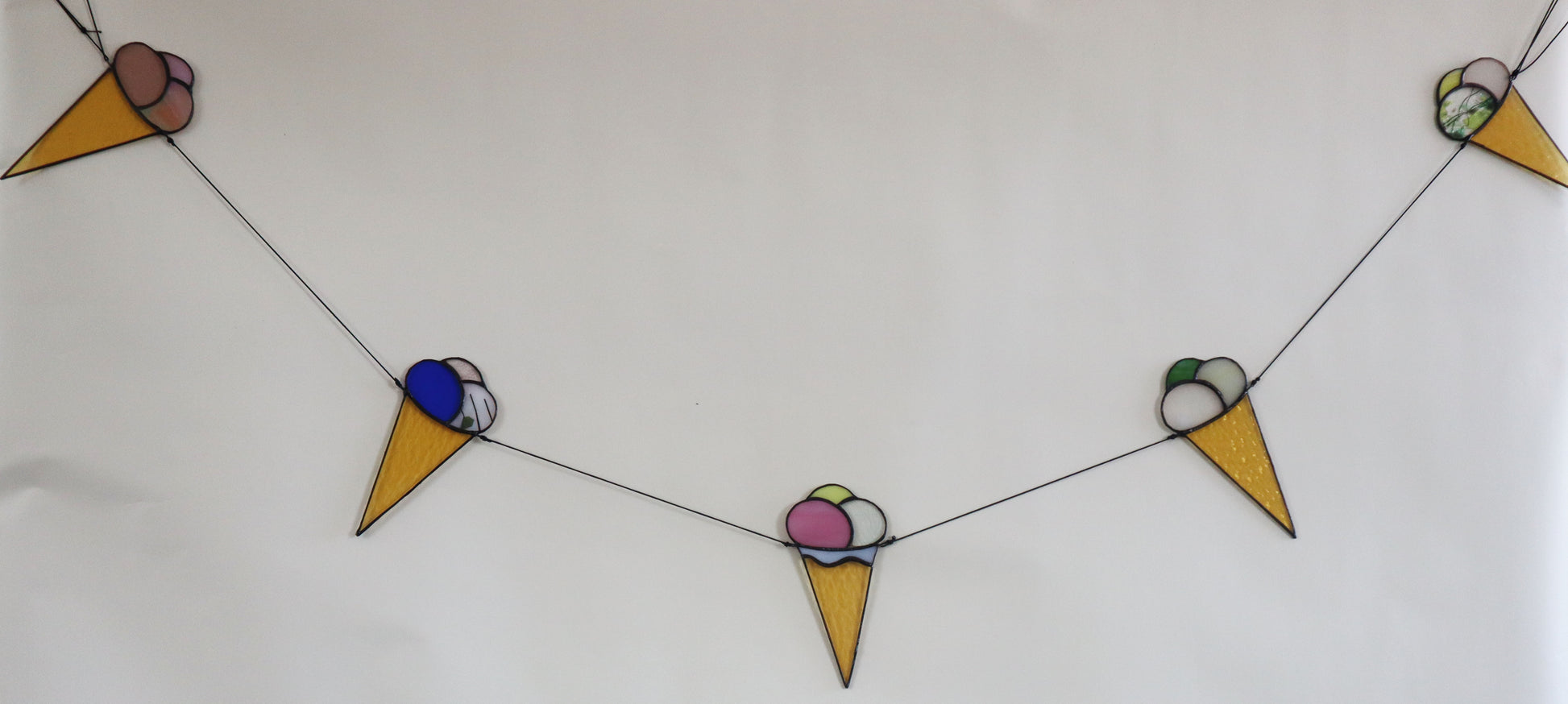 The LF Kaleidoscope Ice Cream Bunting, made of stained glass, showcases delightful ice cream cones and dipped ‘sugar cones’ in three scoops combinations. Choose your favourite colourful flavours. This unique bunting features a string of 5 cone designs each with a unique one-off flavour combo in clear, red, orange, green, blue, stripped, purple, pink, yellow and textured colours. Choose your family favourites. 