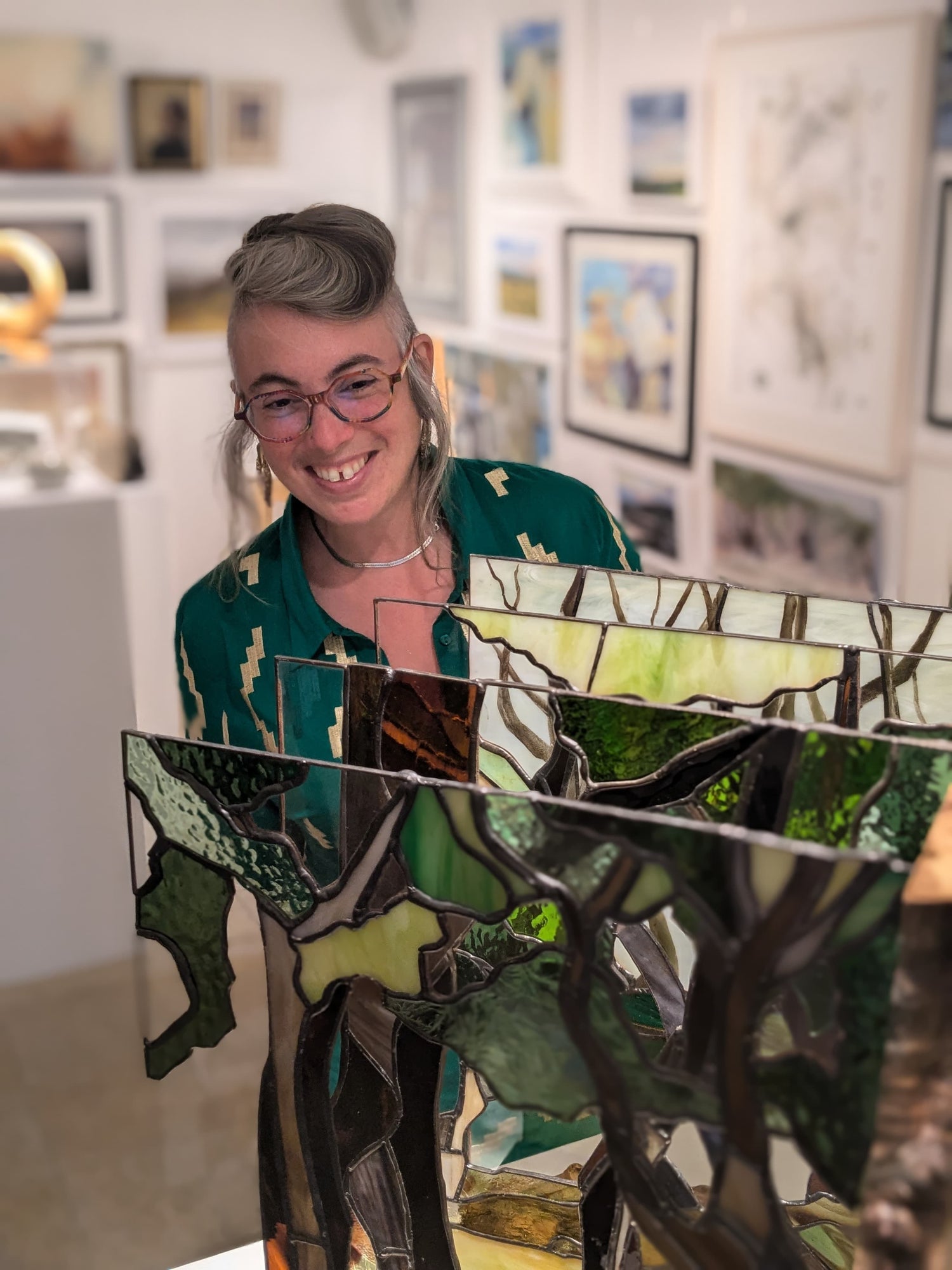 Image of Artist Laura Kriefman at Green Hill Arts Biennale Exhibition opening. Laura is smiling and looking at   the bespoke glass artwork Dartmoor Rainforest. 