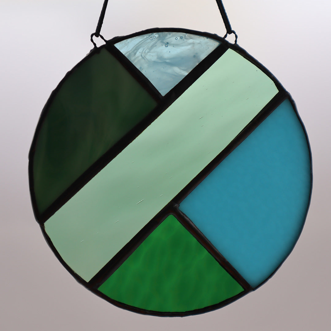 Four distinct pieces from the "Circles, Green" collection by LF Kaleidoscope are showcased against a white backdrop. Each suspended circle displays geometric patterns in hues of green and blue, with diverse textures. They are affixed to black strings for hanging.