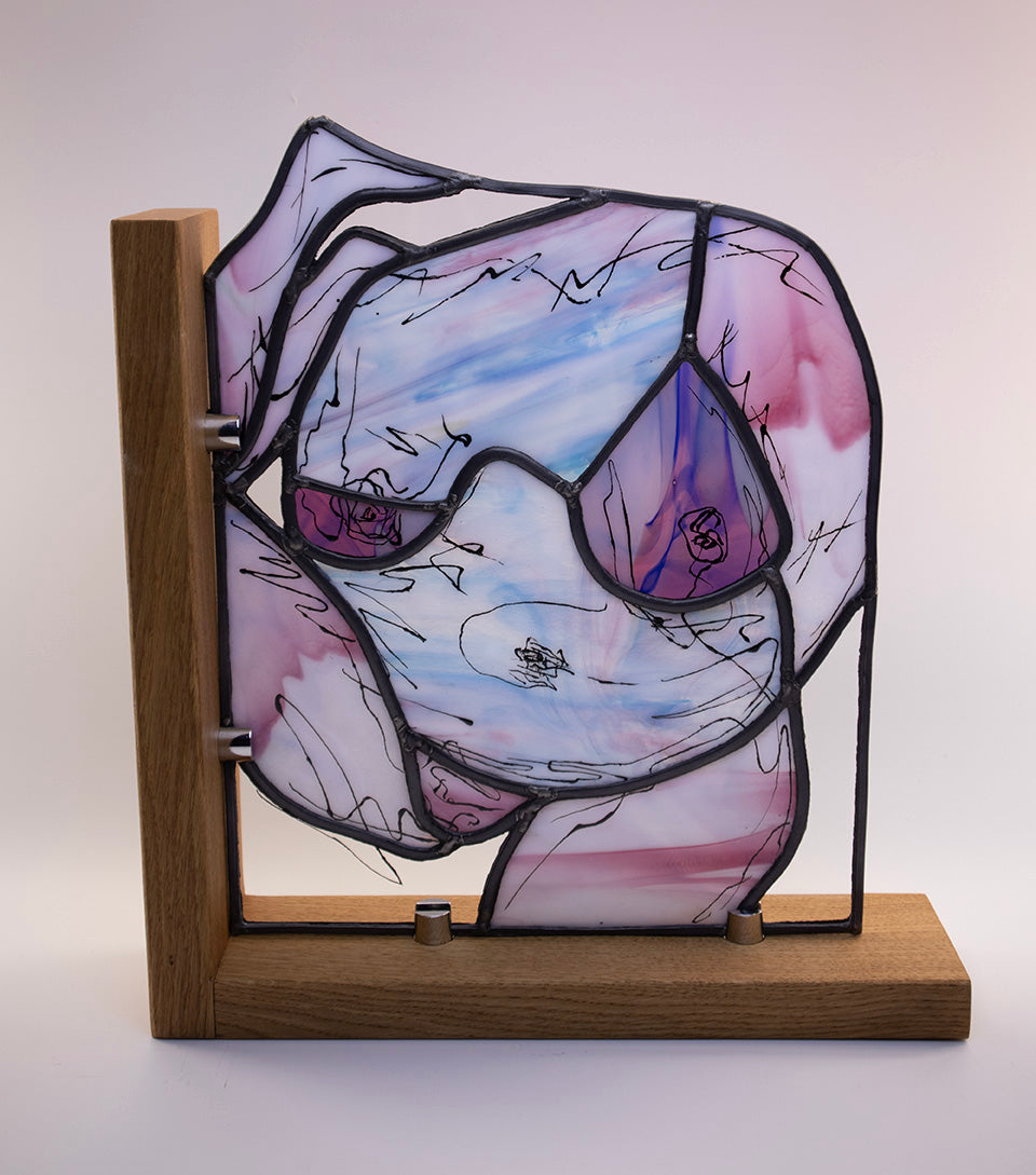 The Lily stained glass artwork, created by LF Kaleidoscope using rare Uroboros Glass, is a Personalized Glass Portrait of Lily capturing her curvacious nude body in magnificent white, pink and blue handmade glass, with extra glass painted calligraphy detail. It’s a great example of a freestanding luxury glass portrait for art collectors. 