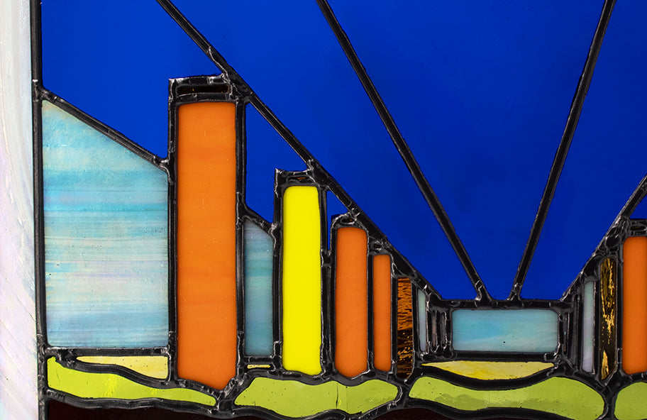 The artwork titled "Neon Fly Over" by LF Kaleidoscope features a stained glass design with geometric forms, including vertical orange and yellow columns set against a deep blue overpass. Black leadlines converge towards the horizon, evoking the perspective of a neon flyover, while the lower section showcases undulating green and purple glass. A playful contemporary artwork celebrating construction and industry artwork, that would look great in any office. 