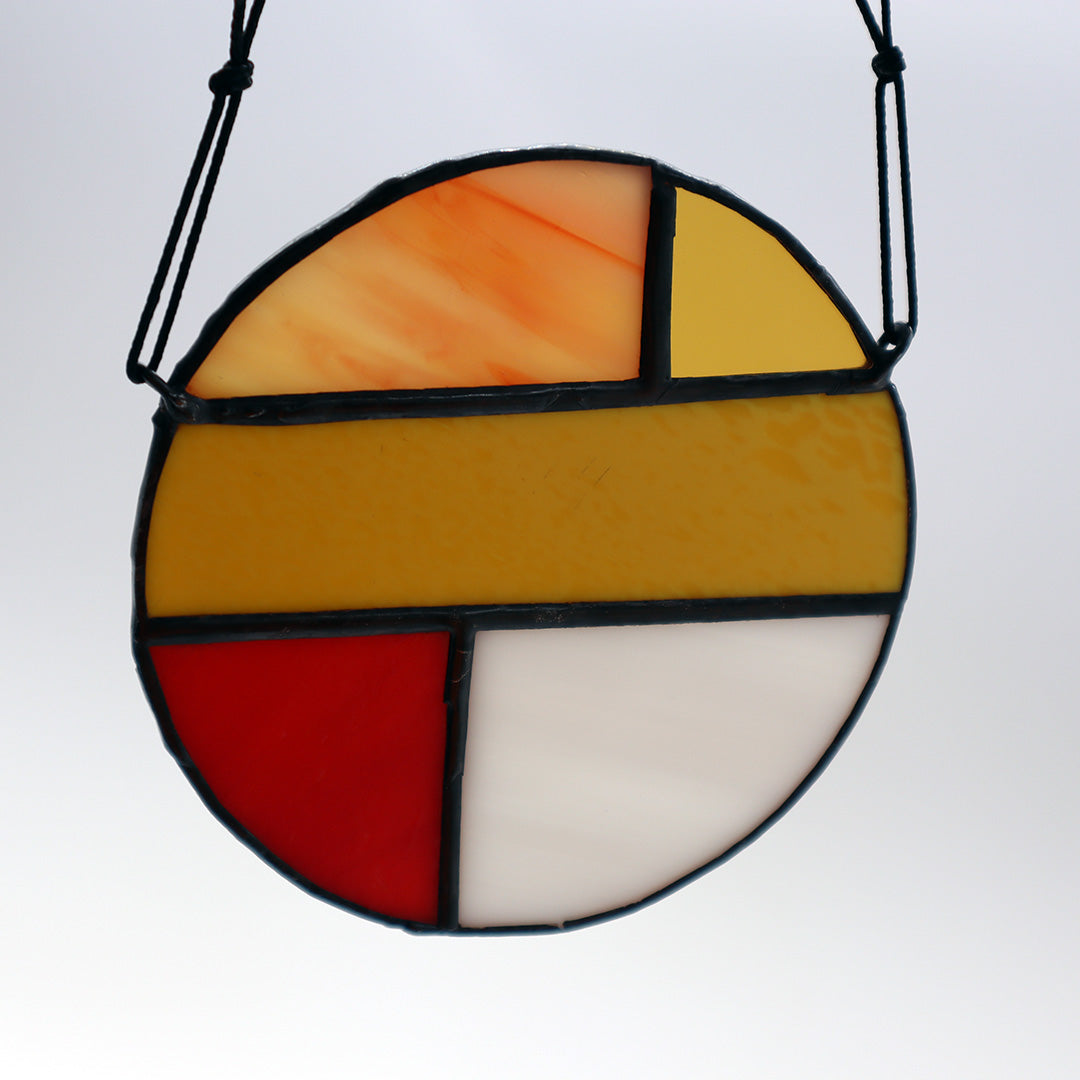 Featuring four distinct pieces, these stained glass circles by LF Kaleidoscope exhibit geometric designs in shades of red, yellow, orange, and white. Each circle is elegantly framed in black and equipped with strings for effortless hanging. They are artistically displayed on a light surface to enhance their vibrant colors.