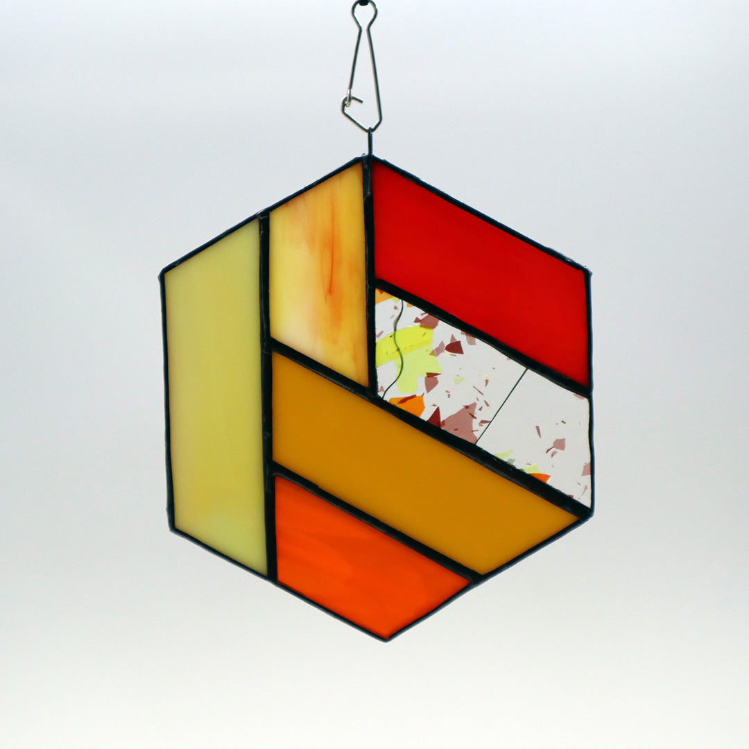 Introducing "Hexagons, Orange" by LF Kaleidoscope—a vintage glass hexagonal stained ornament showcasing a geometric design with vibrant sections of yellow, red, and white, enhanced with delicate orange flecks. Framed in a dark border and elegantly suspended by a wire, this homemade decor piece brings artistic flair to any space.