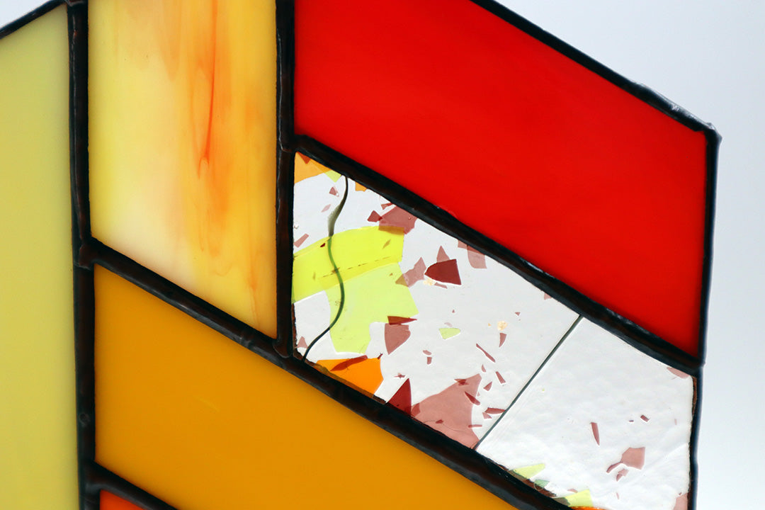 Close up shot of a geometric stained glass piece composed of hexagonal sections featuring red, yellow, orange.