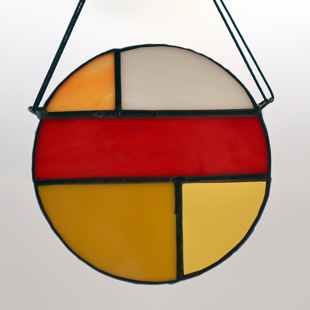 Featuring four distinct pieces, these stained glass circles by LF Kaleidoscope exhibit geometric designs in shades of red, yellow, orange, and white. Each circle is elegantly framed in black and equipped with strings for effortless hanging. They are artistically displayed on a light surface to enhance their vibrant colors.