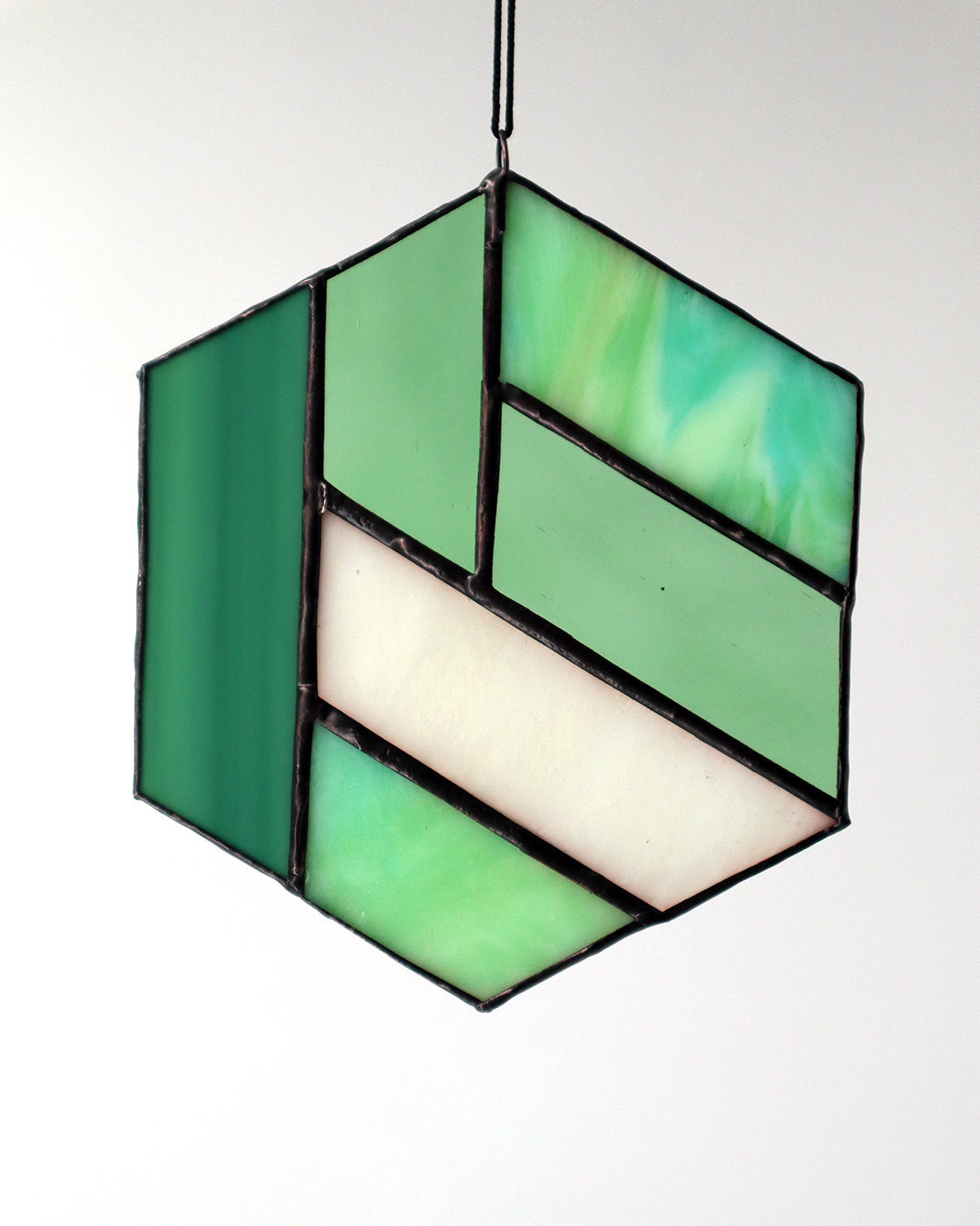 The "Hexagon, Green" ornament by LF Kaleidoscope features a geometric design made from vintage glass with an array of green and clear panels, elegantly hanging against a light background.