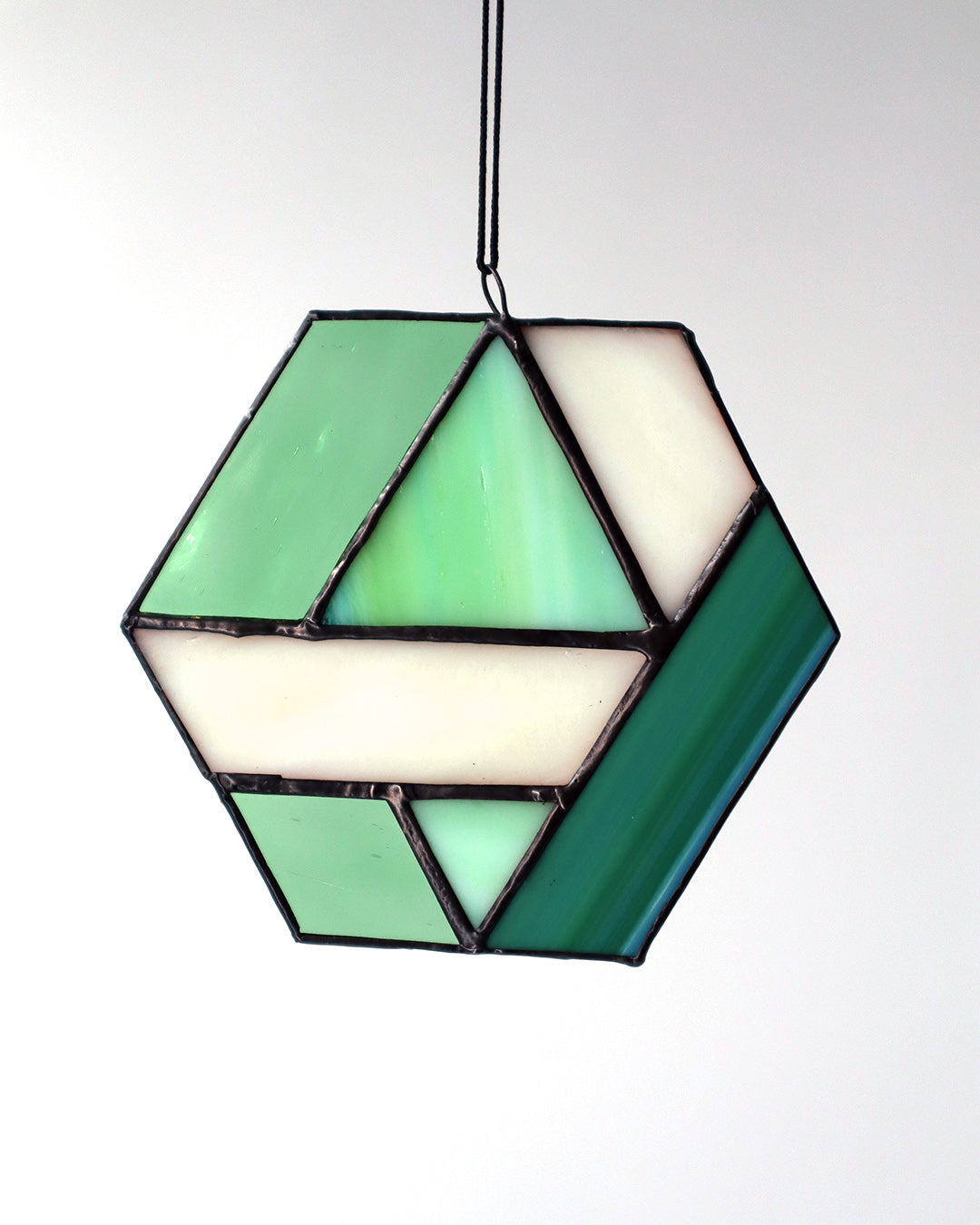 The "Hexagon, Green" ornament by LF Kaleidoscope features a geometric design made from vintage glass with an array of green and clear panels, elegantly hanging against a light background.