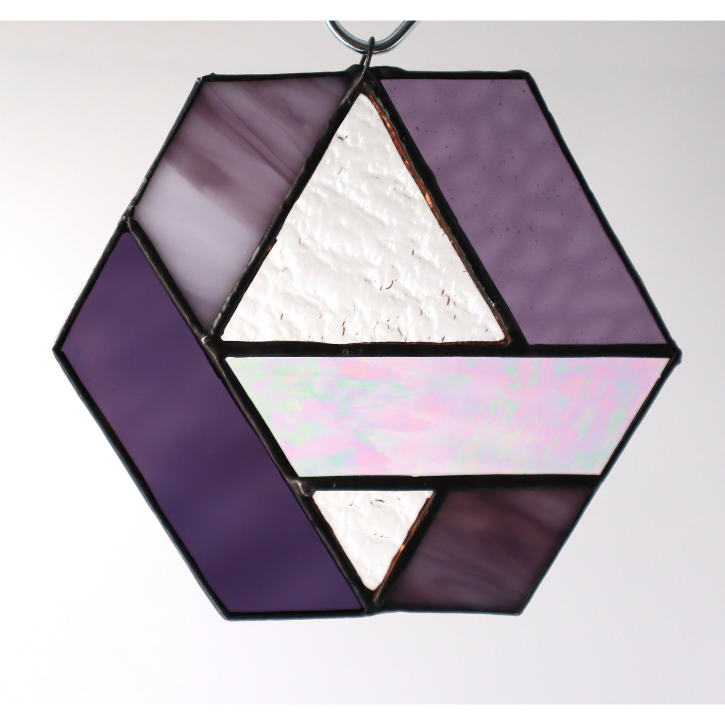 Introducing the "Hexagons, Purple" by LF Kaleidoscope: a stunning geometric-inspired stained glass ornament crafted from vintage glass offcuts. This hexagonal piece showcases a mix of textured lavender, iridescent, and solid shades of purple that hang beautifully against any plain background.